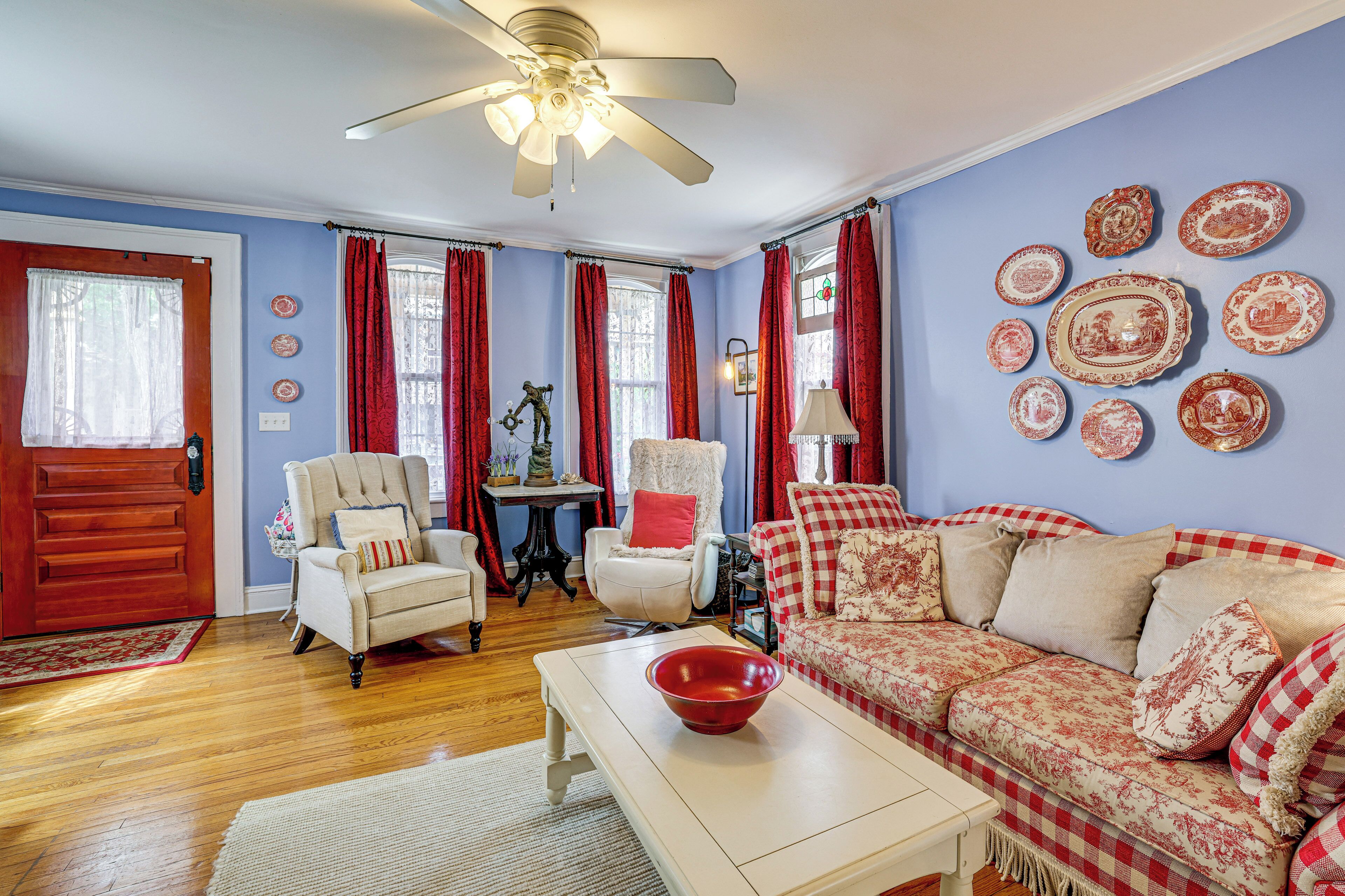A living room with a ceiling fan, a red and white checkered sofa, a white armchair, and a wooden floor.