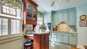 Una cocina con armarios de madera, horno empotrado y ventana con persianas.