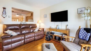 A living room with a brown leather sofa, a wooden coffee table, a television mounted on the wall, and a lamp on a side table.