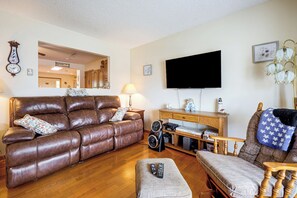 A living room with a brown leather sofa, a wooden coffee table, a television mounted on the wall, and a lamp on a side table.