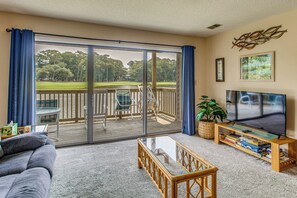 A living room with a large sliding glass door leading to a deck, a flat-screen TV, a coffee table, and a bookshelf. - Near Golf! Waterfront Unit w/ Pool in Sunset Beach (Sunset Beach)