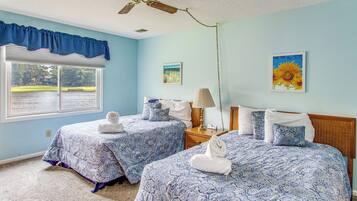 A bedroom with two beds, a ceiling fan, a window with a view of a body of water, and a painting of sunflowers.