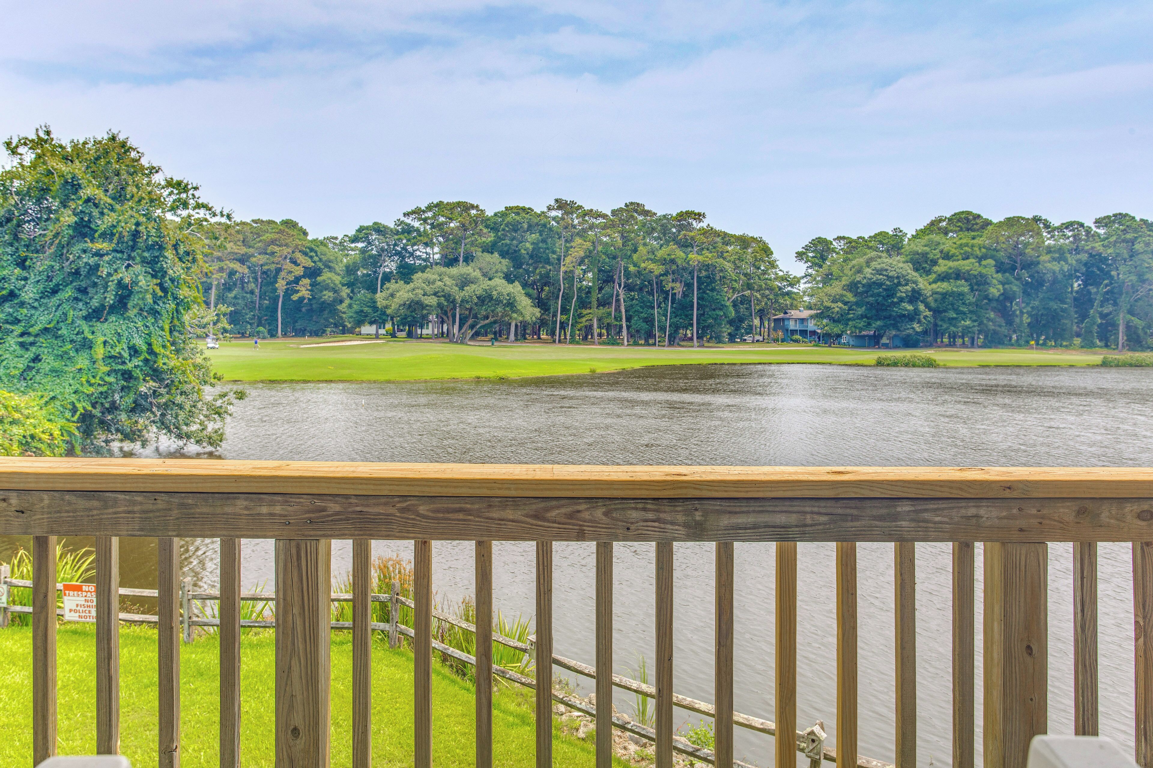 Una terraza de madera con vista a un lago tranquilo y un campo de golf al fondo.