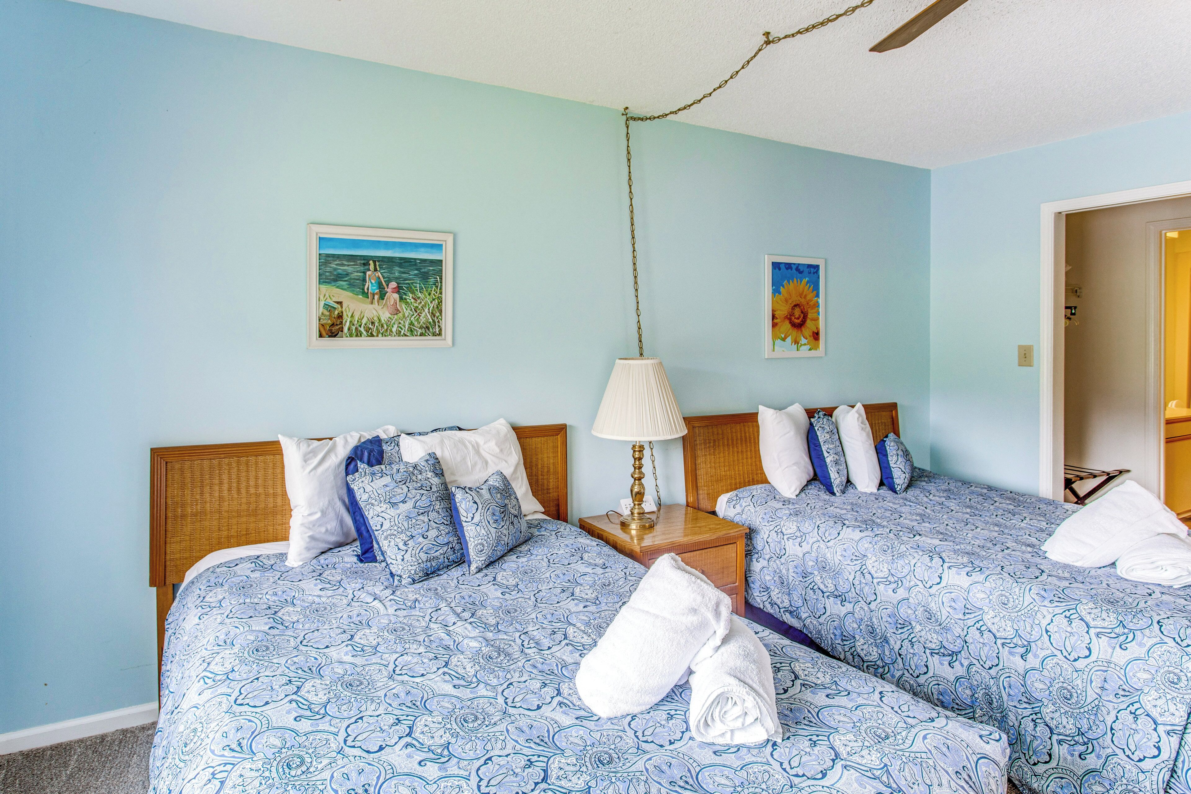 A hotel room with two beds, a nightstand, a lamp, and two wall art pieces.