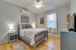 Ein Schlafzimmer mit einem Bett, Nachttischen, einer Klimaanlage, einem Deckenventilator und einem Fenster mit Vorhängen.