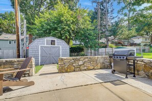 Un jardin avec un mur en pierre, un barbecue, un banc en bois et un abri de jardin.
