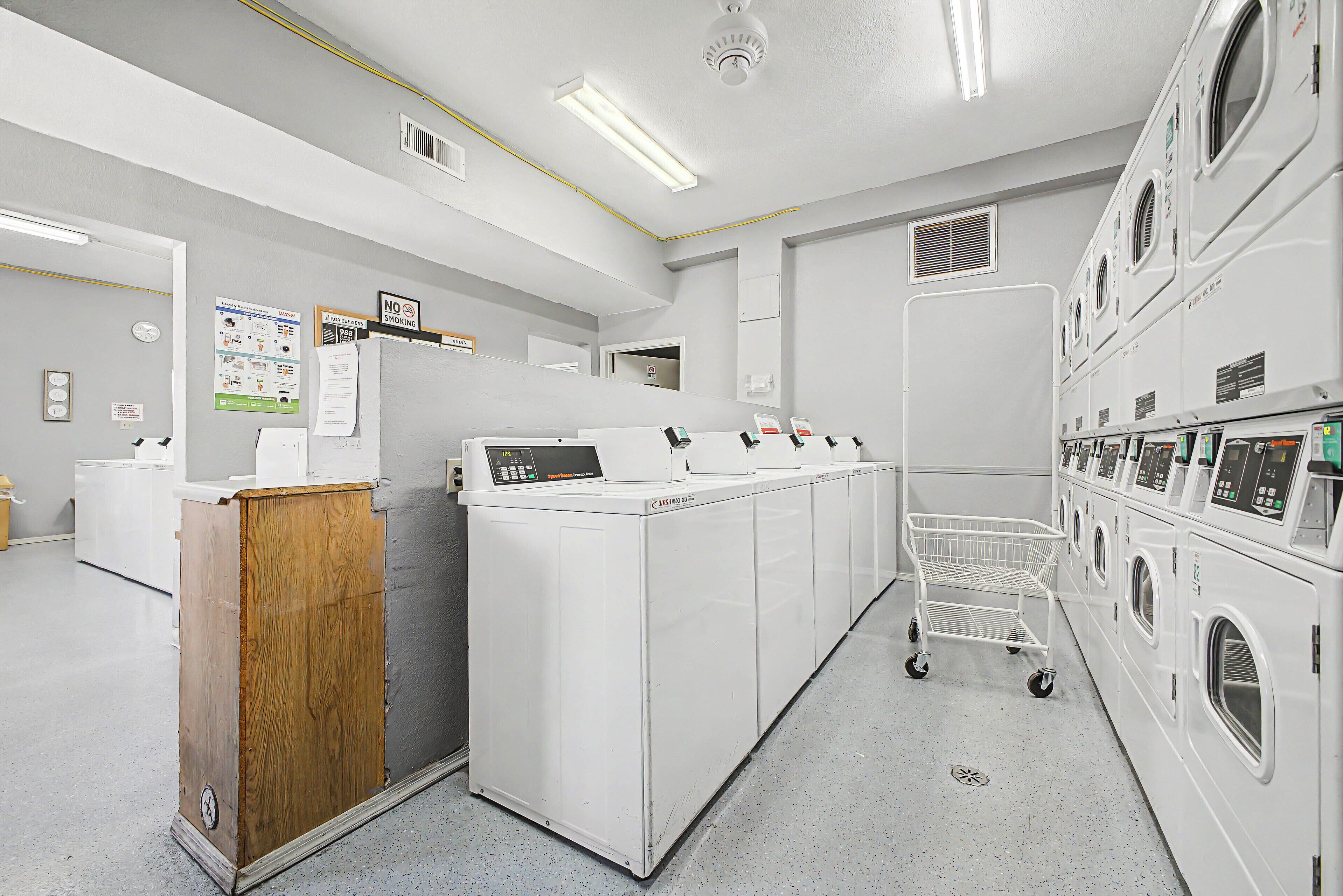 A laundry facility with multiple washing machines, a wooden counter, and a cart.