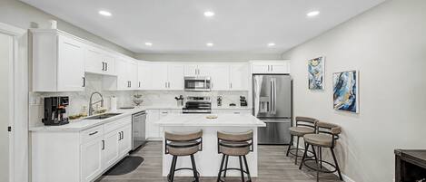 A modern kitchen with white cabinetry, stainless steel appliances, and a central island with bar stools.