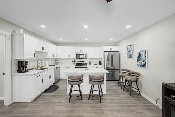 A modern kitchen with white cabinetry, stainless steel appliances, and a central island with bar stools. - Pool & Hot Tub Access! Superstition Mtn Condo (Apache Junction)