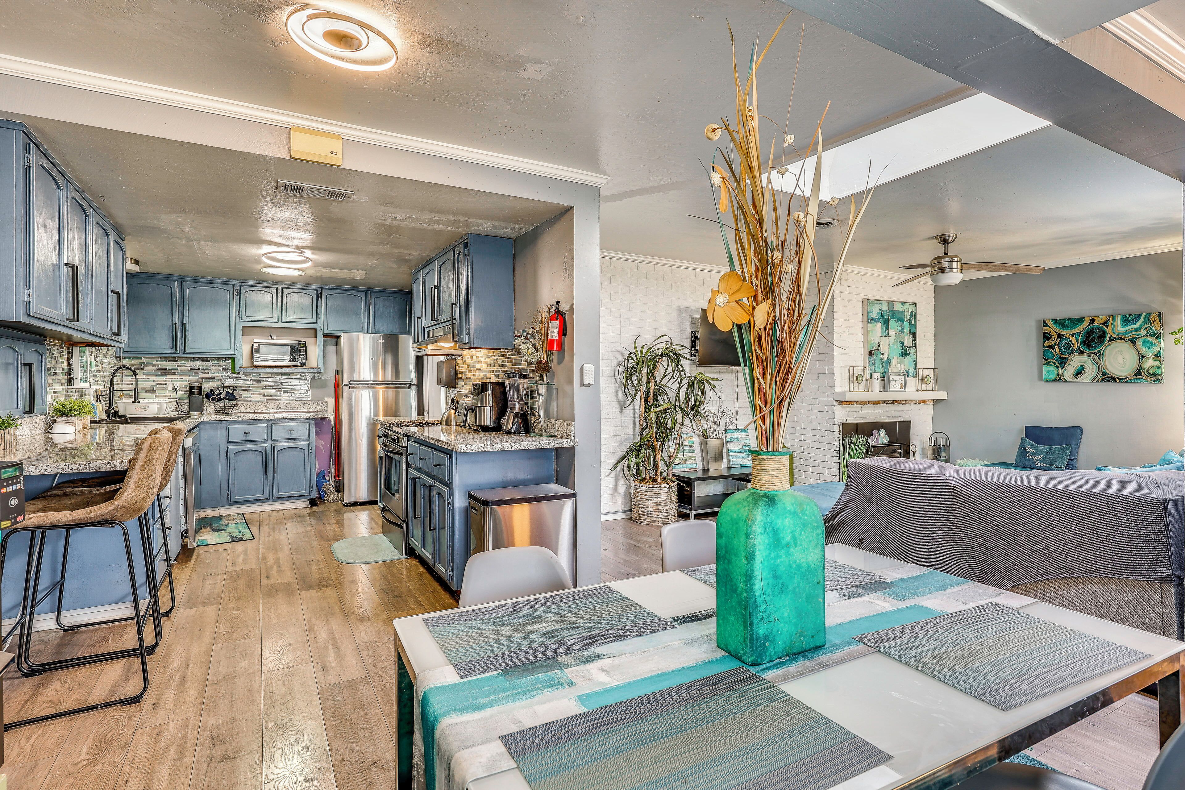 A modern kitchen with blue cabinets, stainless steel appliances, and a dining area with a table covered by a patterned tablecloth.