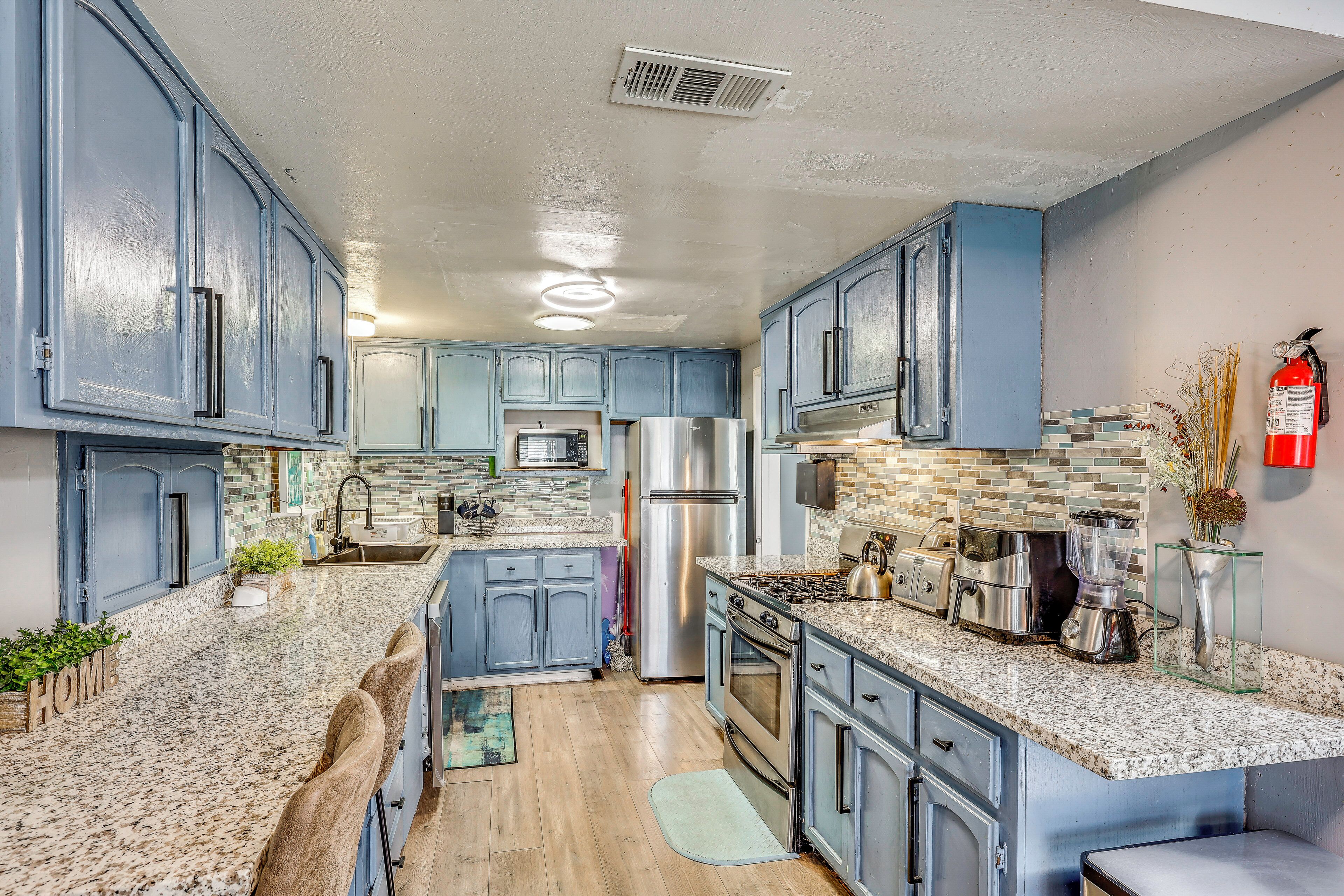 A kitchen with blue cabinets, a stainless steel refrigerator, a microwave, a stove, and a sink.