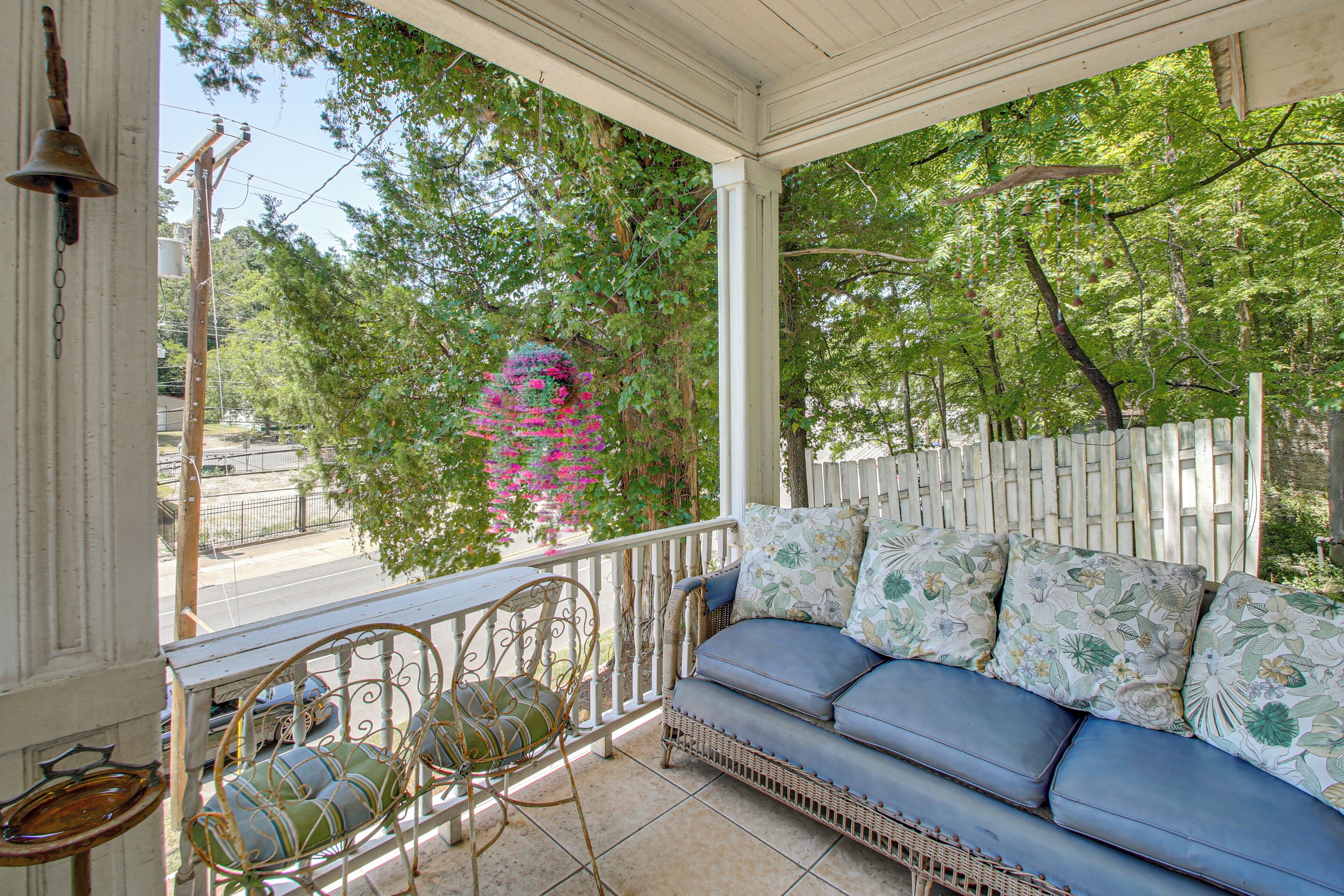 A covered porch with a blue sofa and wicker chairs, surrounded by trees and a white fence.