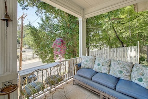 A covered porch with a blue sofa and wicker chairs, surrounded by trees and a white fence. - Walk to Bathhouse Row! Historic Gem w/ Yard (Hot Springs)