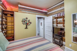 A bedroom with a bed, a wall-mounted shelf with books, a door with a 'WASH' sign, and a decorative tree. - Walk to Bathhouse Row! Historic Gem w/ Yard (Hot Springs)