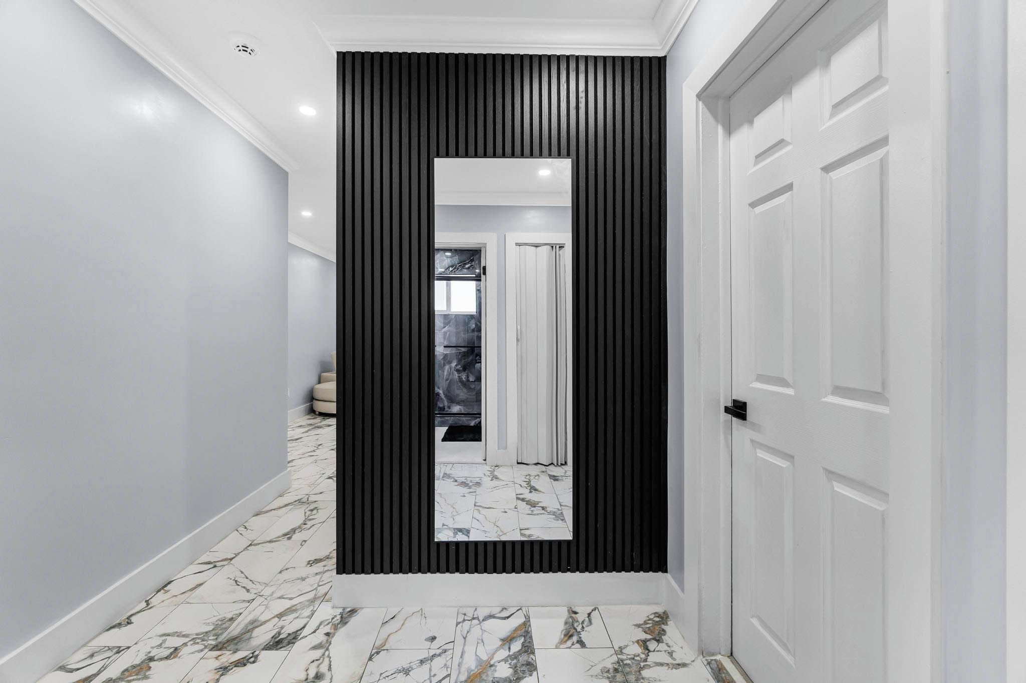 Um corredor com painel vertical preto, portas brancas e piso de mármore.