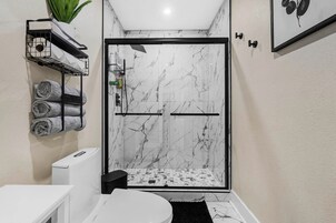 A modern bathroom with a shower, marble walls, a towel rack, and a toilet.
