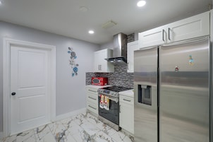 A modern kitchen with white cabinetry, a stainless steel refrigerator, a red microwave, and a tiled backsplash.