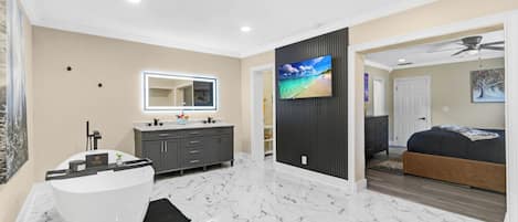 A modern bathroom with a freestanding bathtub, a vanity with a mirror, and a television mounted on a wall.