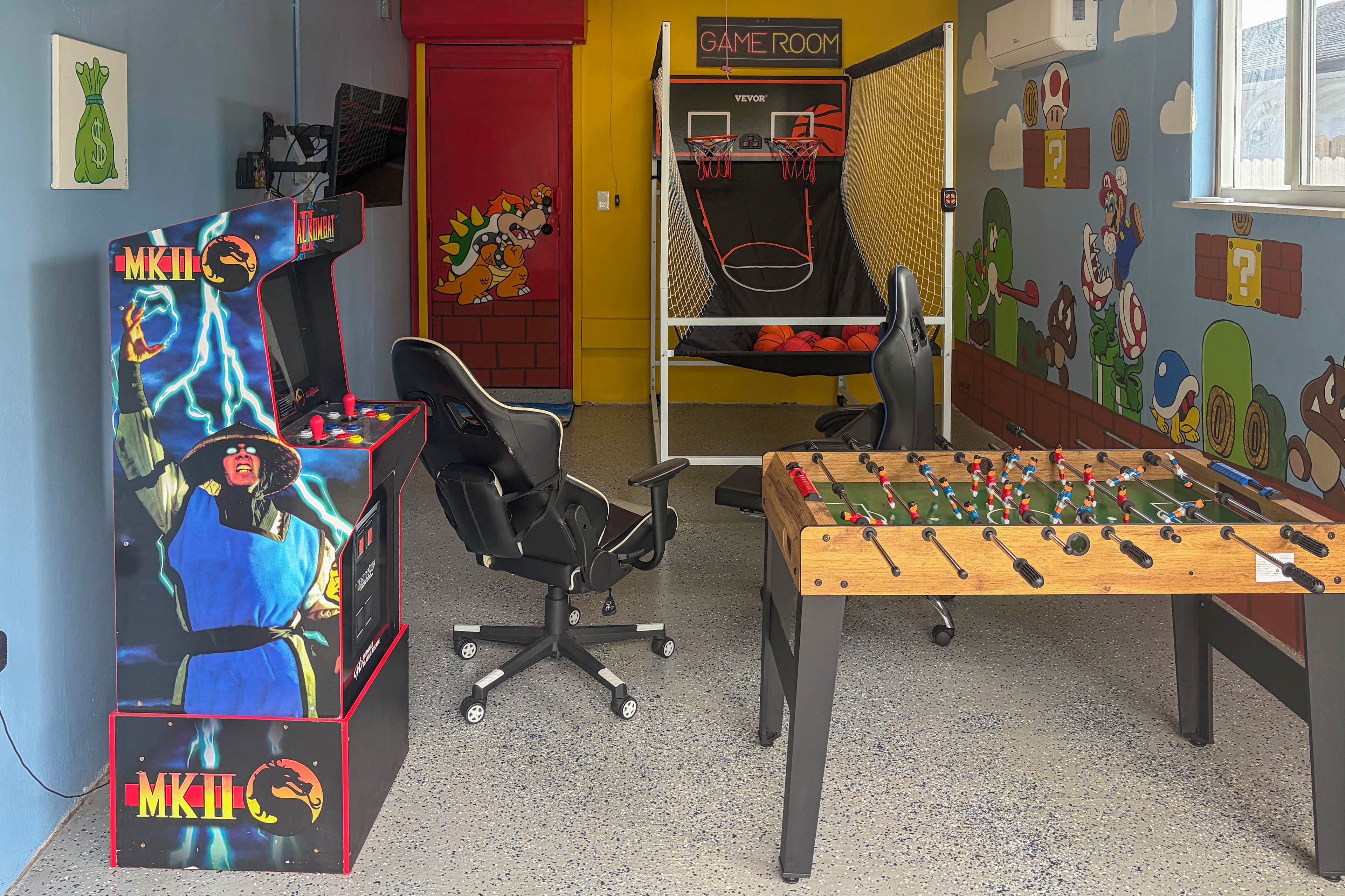 A room with a foosball table, a gaming chair, and arcade machines.