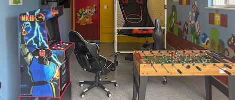 A room with a foosball table, a gaming chair, and arcade machines.