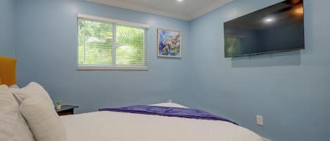 A bedroom with a bed, a ceiling fan, a TV mounted on the wall, and a window with blinds.