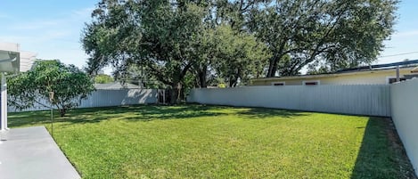 Un jardin avec une clôture blanche, un arbre et une terrasse en béton.