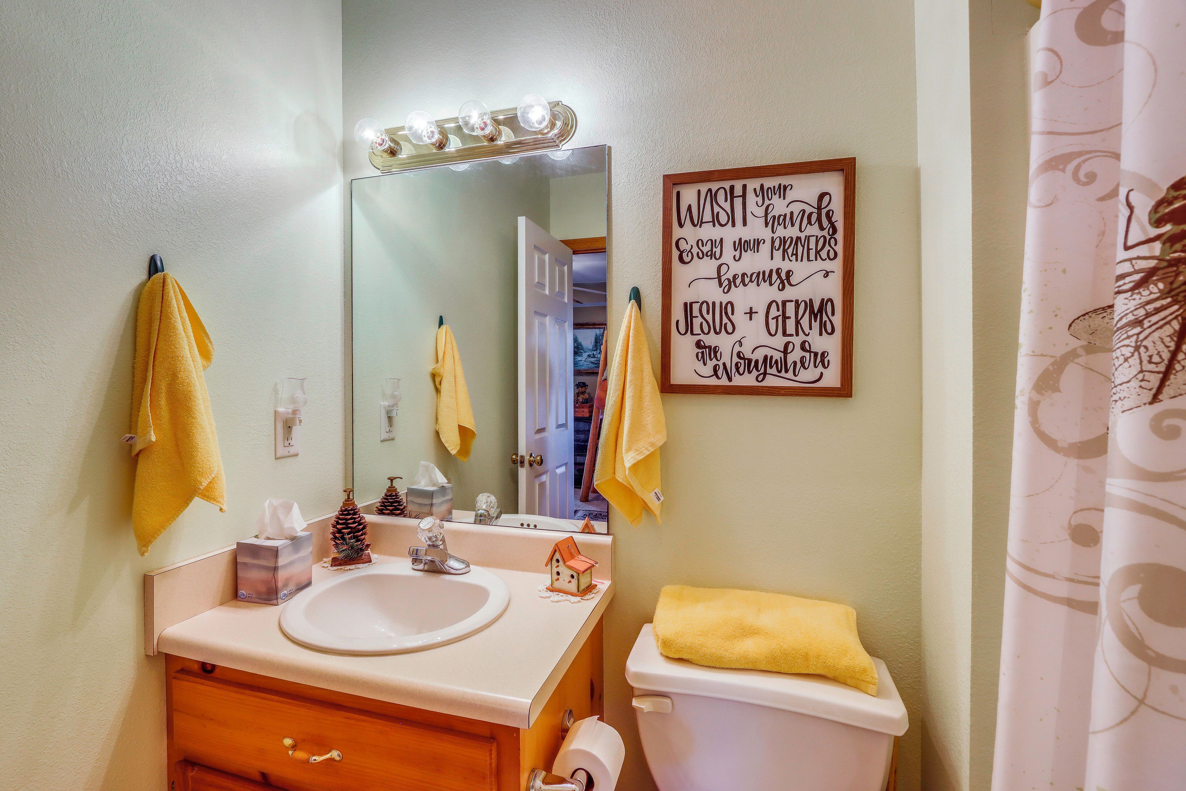 A bathroom with a white sink, a mirror, a yellow towel, a toilet, and a sign on the wall.