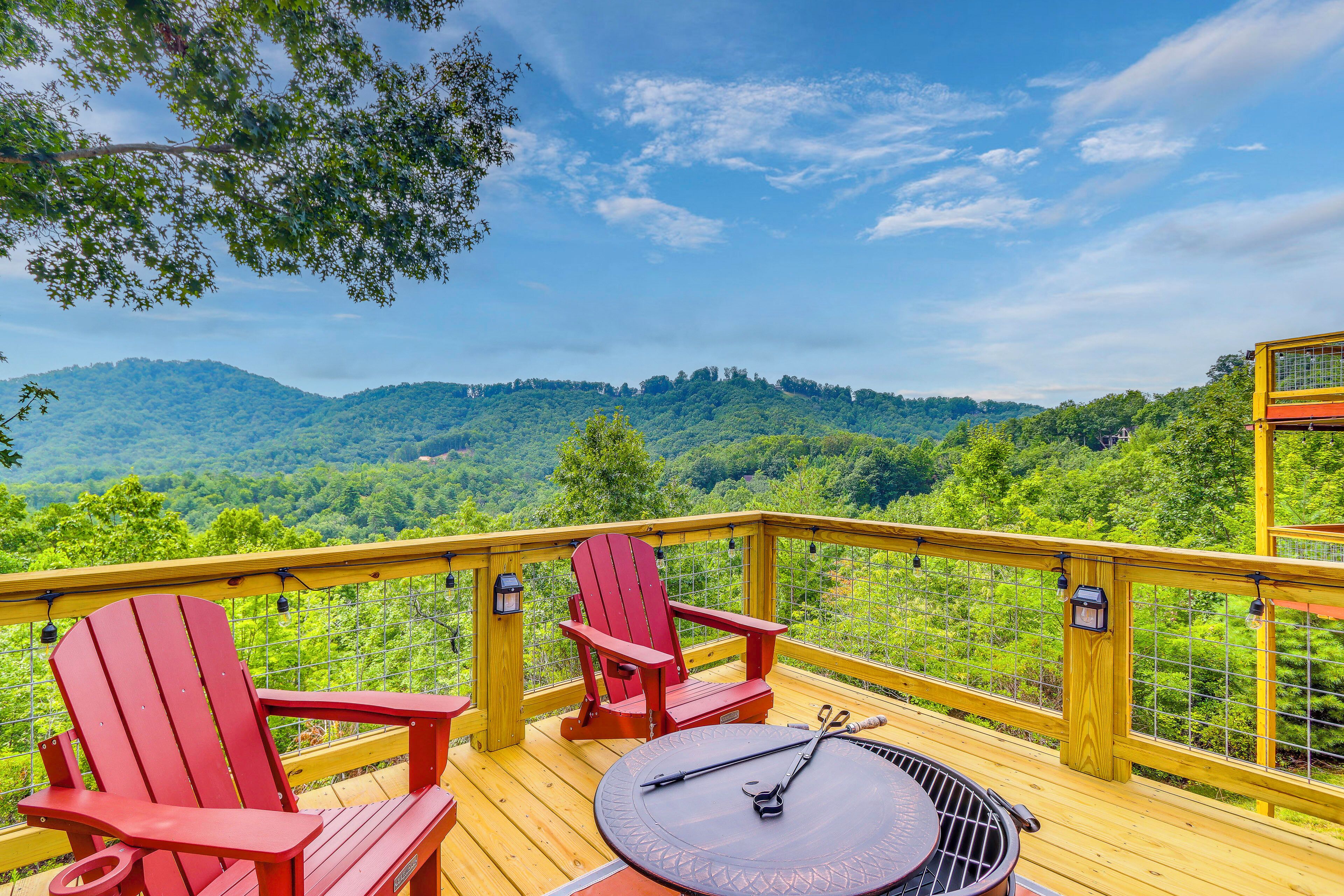 A deck with two red Adirondack chairs, a round table, and a grill.