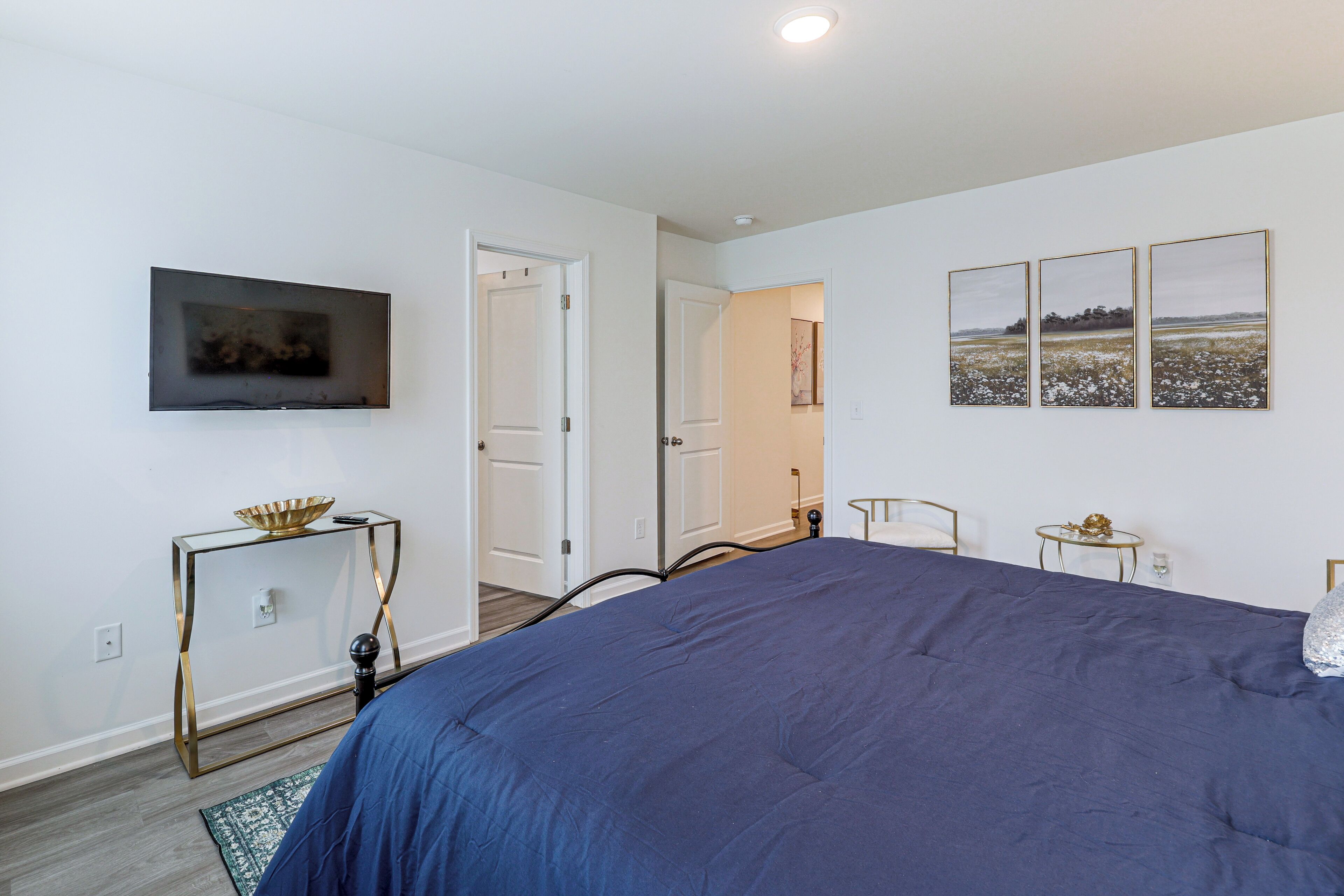 A bedroom with a large bed, a television mounted on the wall, and a door leading to another room.