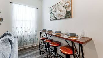 Un comedor con una mesa de madera, cuatro taburetes y un cuadro de flores en la pared.