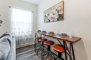 A dining area with a wooden table, four stools, and a painting of flowers on the wall.