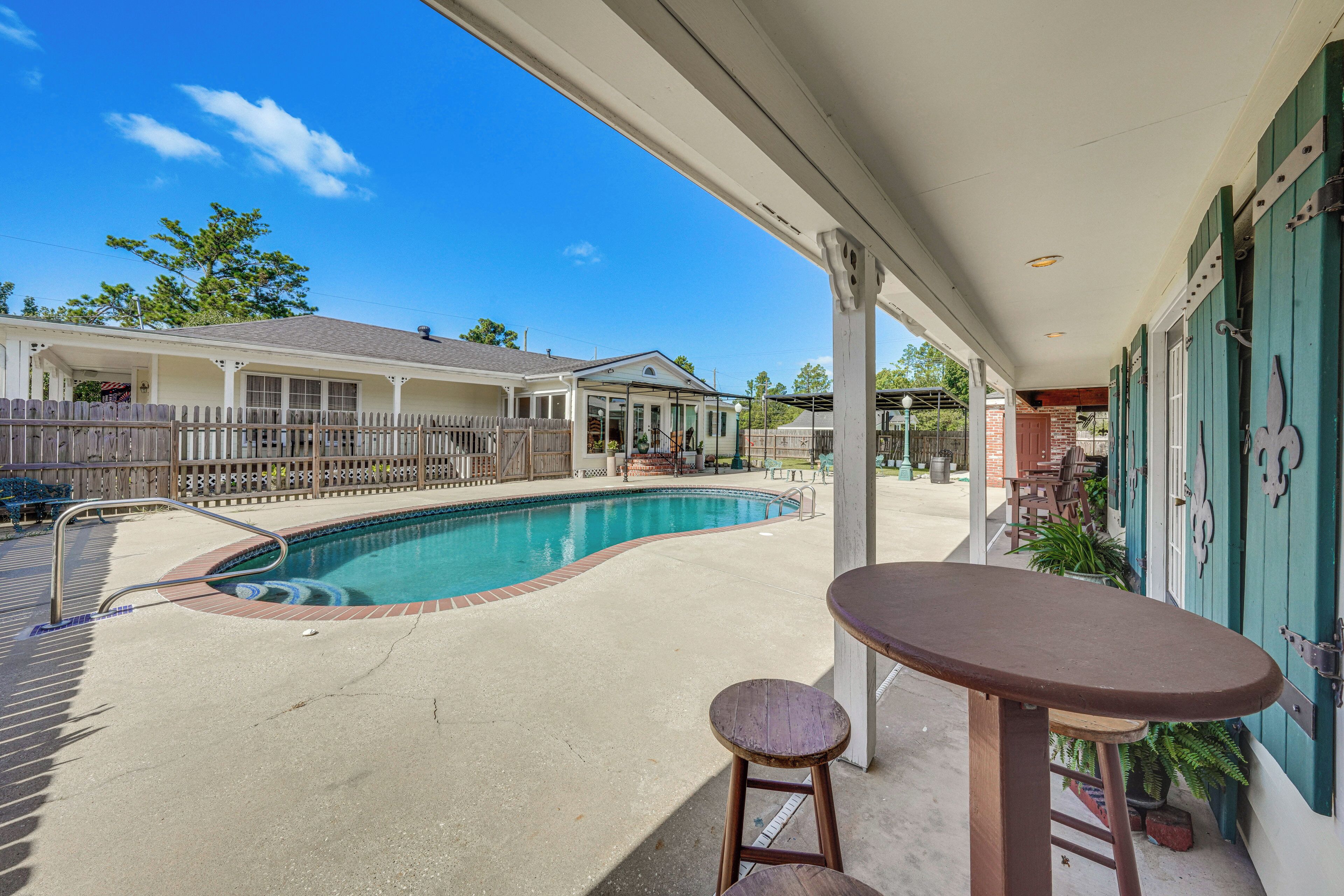 A swimming pool with a patio area, a covered seating area, and a view of a residential building in the background.