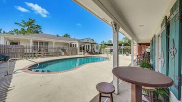 A swimming pool with a patio area, a covered seating area, and a view of a residential building in the background.