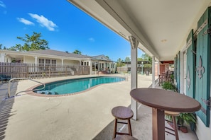 A swimming pool with a patio area, a covered seating area, and a view of a residential building in the background.