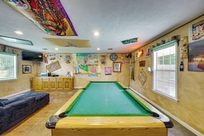 A pool table with a green felt surface, wooden cabinets, and a television on the wall.