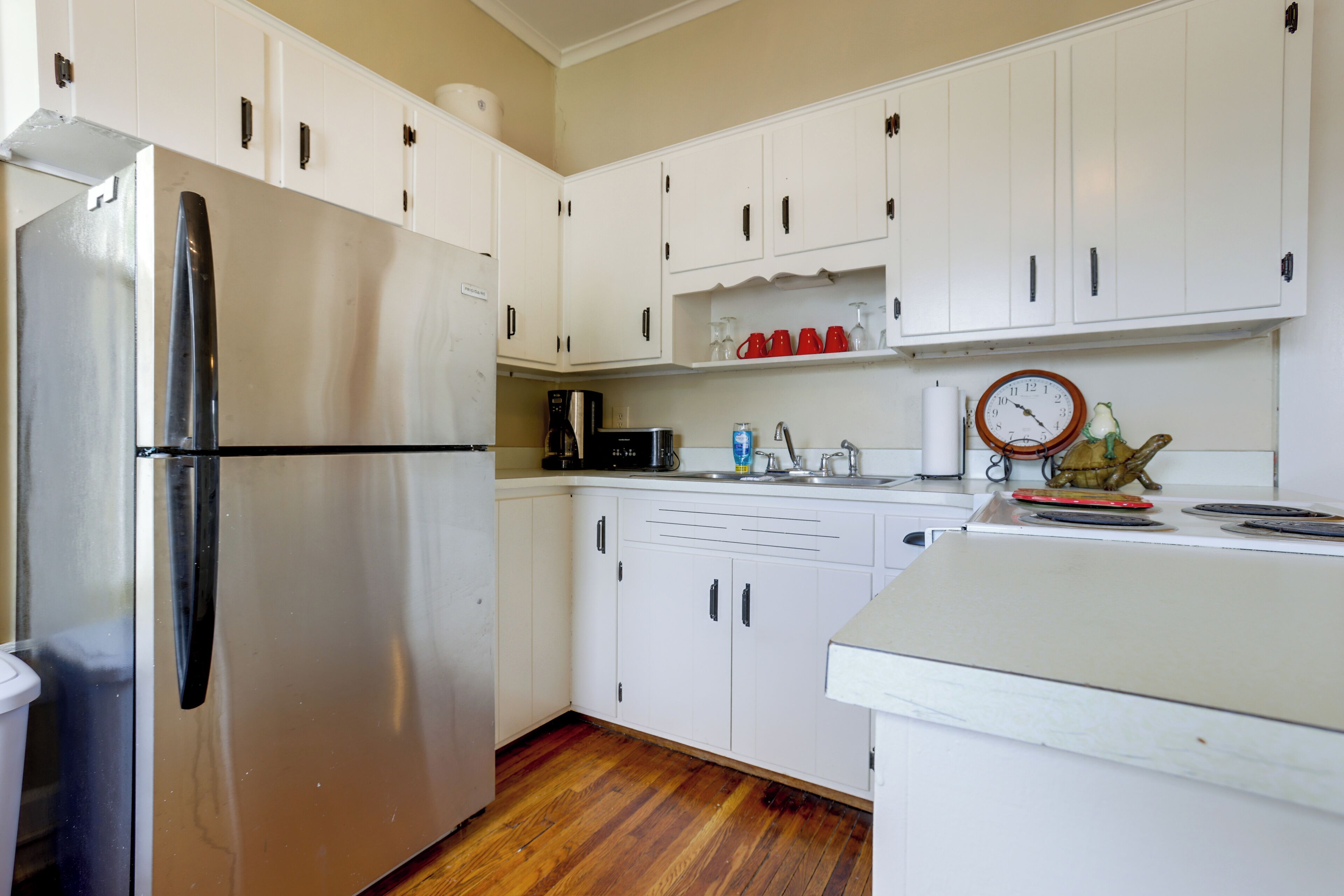 A kitchen with white cabinets, a stainless steel refrigerator, a coffee maker, and a clock on the wall.