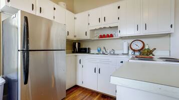 A kitchen with white cabinets, a stainless steel refrigerator, a coffee maker, and a clock on the wall.