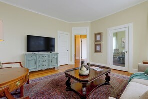 Un salon comprenant un téléviseur, une table basse en bois, un tapis à motifs et un coin repas avec une table et des chaises.