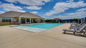 Une piscine avec des chaises longues, un espace de détente couvert et un bâtiment doté d’un toit en pente.