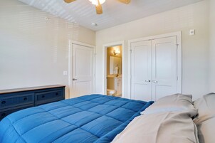 Un dormitorio con colcha azul, cabecera de madera y ventilador de techo blanco.