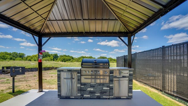Un espace barbecue extérieur doté d’un toit en métal, d’éléments décoratifs en pierre et d’un gril.