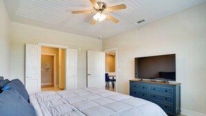 Une chambre à coucher comprenant un lit, une commode, un téléviseur et un ventilateur de plafond.