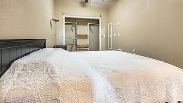 A bedroom with a large bed, a ceiling fan, a walk-in closet, and a full-length mirror.