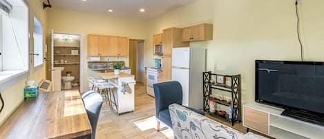 A modern kitchen with a dining area, a living room with a flat-screen TV, and a ceiling fan.