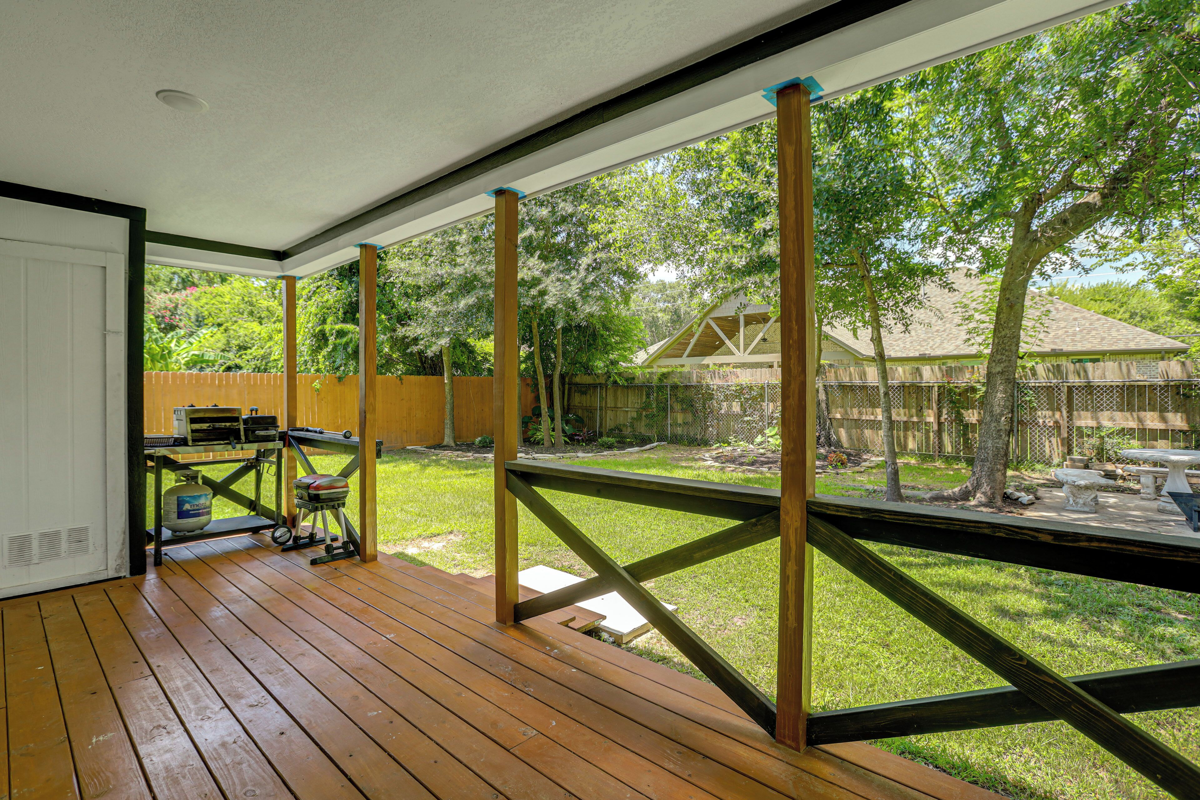 A wooden deck with a view of a backyard, a barbecue grill, and a fenced area.