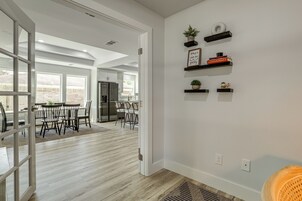 Uma cozinha moderna com armários brancos, uma área de refeições com mesa e cadeiras, e um corredor que leva a uma sala de estar.