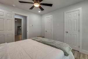 Quarto com cama, ventilador de teto e portas brancas.