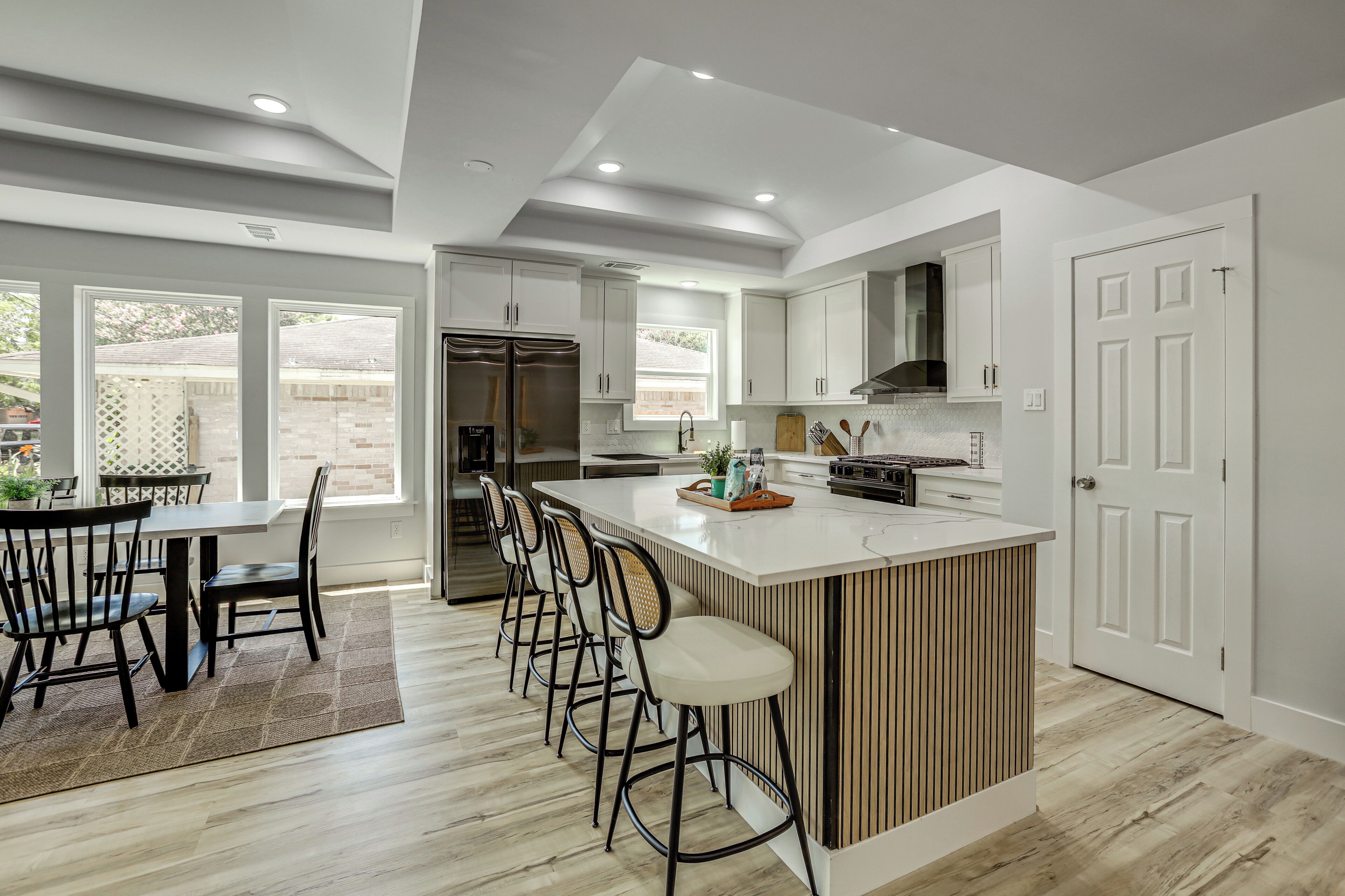 A modern kitchen with a central island, bar stools, and a dining area with a table and chairs.