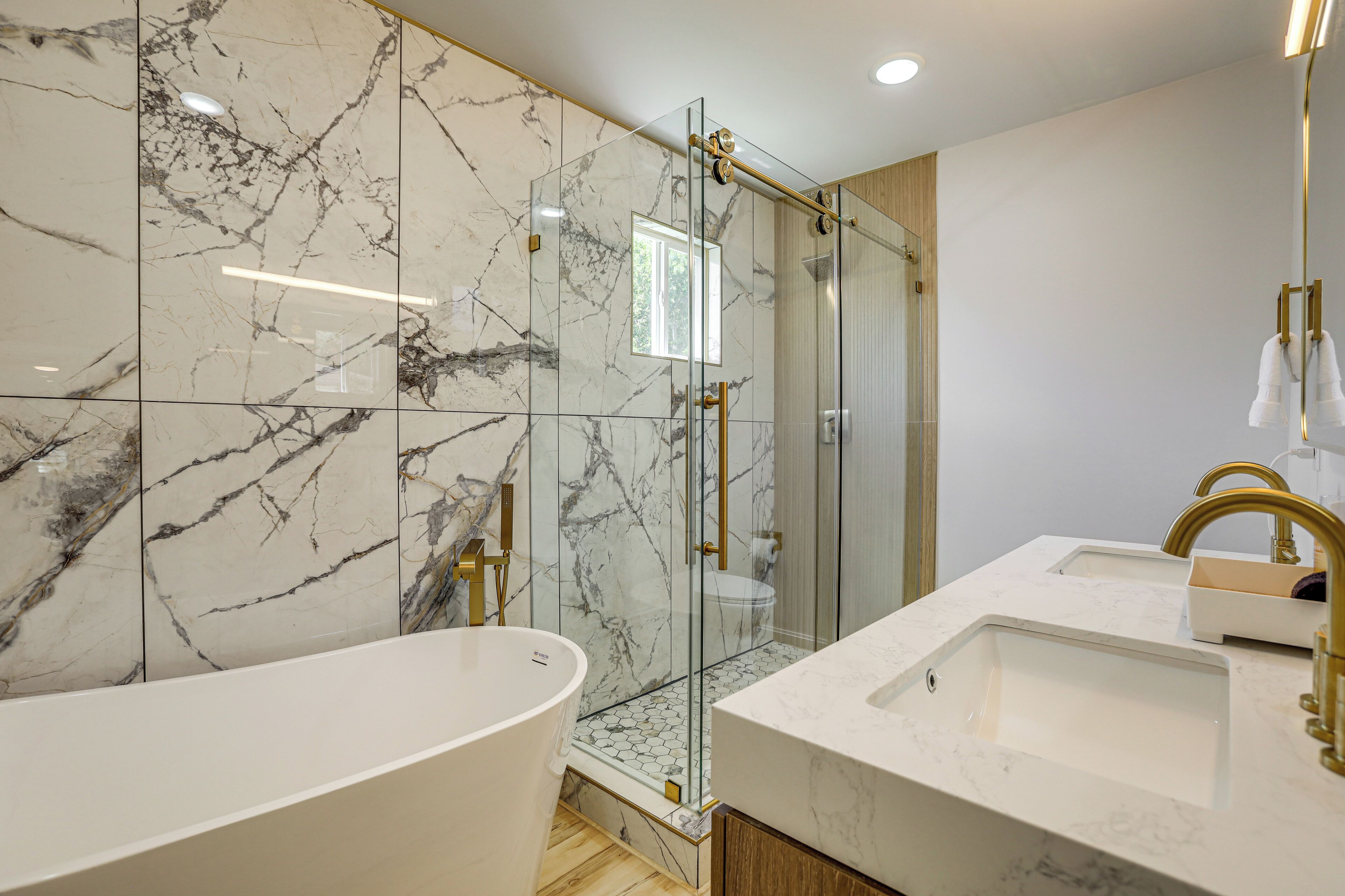 A modern bathroom with a freestanding bathtub, a glass-enclosed shower, and a vanity with a gold faucet.