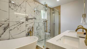 A modern bathroom with a freestanding bathtub, a glass-enclosed shower, and a vanity with a gold faucet.